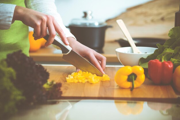 Unbekannte menschliche Hände kochen in der Küche. Frau, die gelbe Paprika schneidet. Gesunde Mahlzeit und vegetarisches Lebensmittelkonzept.