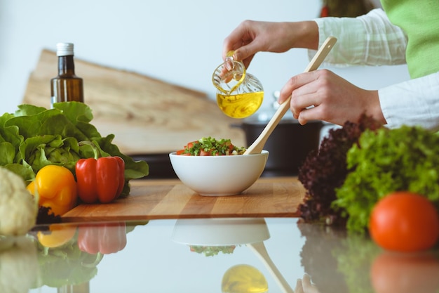 Unbekannte menschliche Hände kochen in der Küche. Frau ist mit Gemüsesalat beschäftigt. Gesunde Mahlzeit und vegetarisches Lebensmittelkonzept.