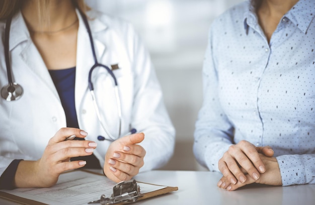 Unbekannte Ärztin und ihre Patientin sehen sich die aktuellen medizinischen Testergebnisse der Patientin an, während sie gemeinsam am Schreibtisch im Schrank einer Klinik sitzen. Ärztin benutzt ein Klemmbrett und a