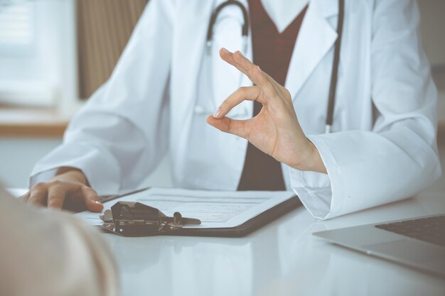 Unbekannte Ärztin und Patientin diskutieren etwas, während sie in der Klinik am Tisch sitzen, Nahaufnahme. Medizin-Konzept.