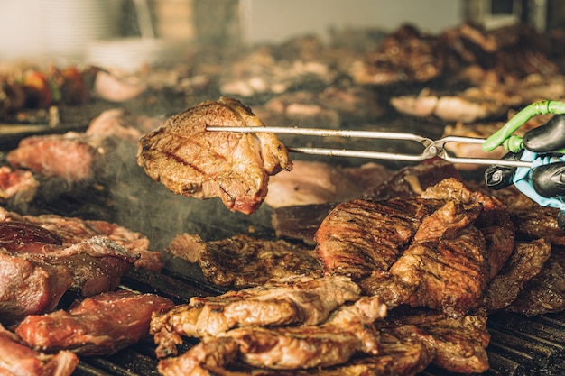 Unbekannter Koch, der mit einer Fleischzange Fleischstücke vom Grill nimmt.