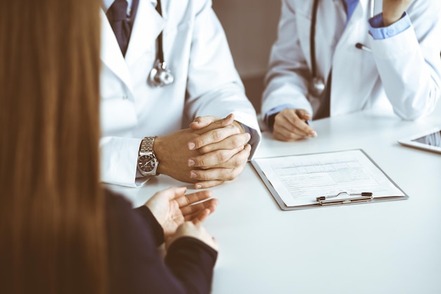 Unbekannter männlicher Arzt, der seiner geduldigen Frau zuhört, während er in einer modernen Klinik sitzt. Perfekter medizinischer Service, Medizinkonzept während der Coronavirus-Pandemie. Covid 2019.