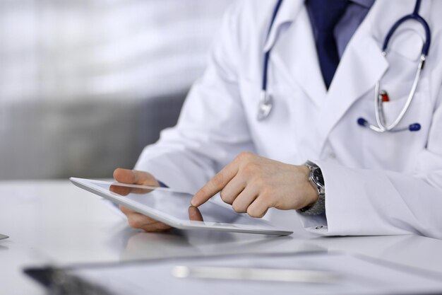 Unbekannter männlicher Arzt sitzt und arbeitet mit Tablet-Computer in der Klinik an seinem Arbeitsplatz Nahaufnahme Junger Arzt bei der Arbeit Perfektes medizinisches Dienstmedizin-Konzept