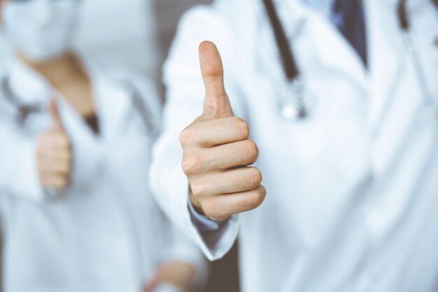 Unbekannter Mandoktor und eine Frau stehen als Team aufrecht und zeigen das Ok-Zeichen mit den Daumen nach oben in einer modernen Klinik Medizinkonzept während der Coronavirus-Pandemie Covid 2019