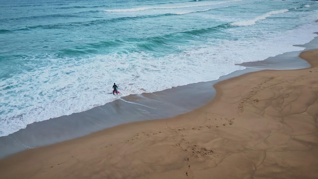 Unbekannter Surfer betritt das Meer. Luftaufnahme eines Surfboarders, der sein Brett aufs Wasser legt