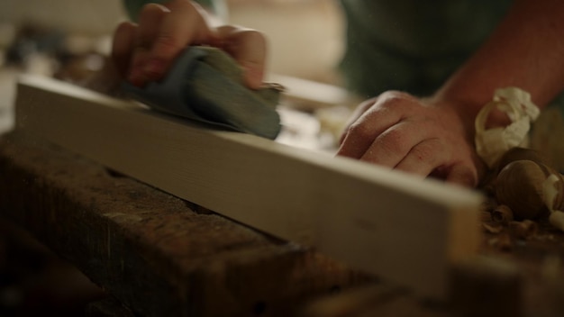 Unbekannter Zimmermann mit Schleifpapier in einer Tischlerwerkstatt Unerkannter Holzarbeiter reinigt eine Holzplatte im Studio Handwerker bereitet Holz für das Produkt im Innenraum vor