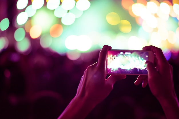 undeutlicher bunter Hintergrund der Hand intelligentes Telefon halten, um die Fotoleute zu nehmen, die im Konzert gedrängt werden.