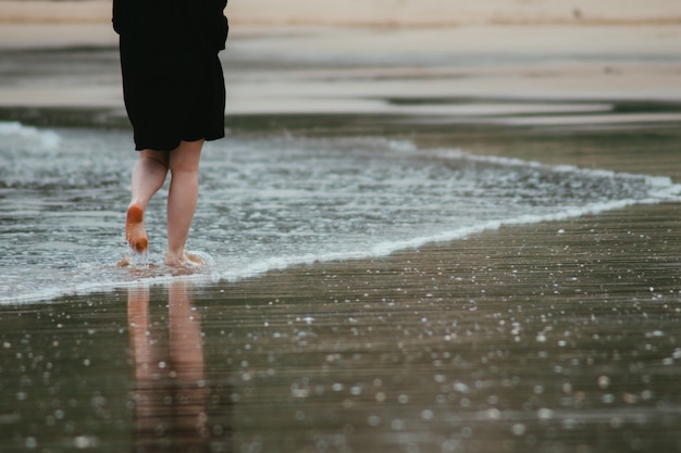 Unerkennbare Frau, die an einem bewölkten Tag am Sandstrand spazieren geht