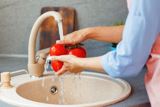 Unerkennbare Frau, die frische Tomaten im Waschbecken wäscht