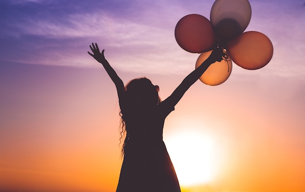 Unerkennbare Frau, die Hände erhebt und Luftballons hält, während sie den malerischen Sonnenuntergang genießt enjoying