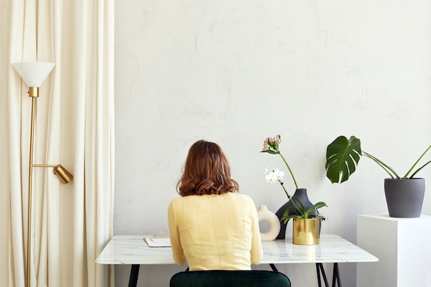 Unerkennbare Frau, die zu Hause mit Blumen am Tisch sitzt