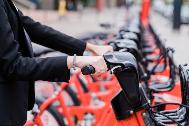 Unerkennbare Geschäftsfrau, die auf der Straße der Stadt auf dem Weg zur Arbeit ein gemeinsames Elektrofahrrad mietet?