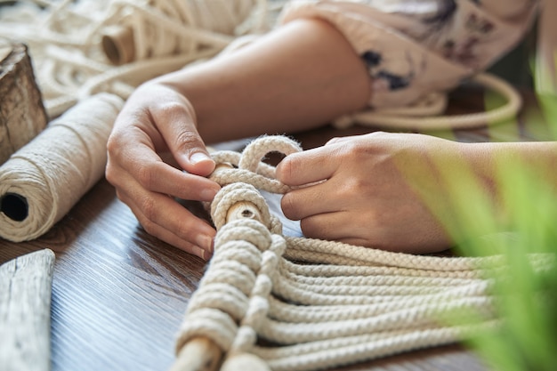 Foto unerkennbare junge frau hände, die an makramee in einem ruhigen arbeitsbereich arbeiten