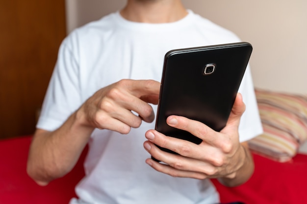 Unerkennbare Person, die ein Tablet in seinem Schlafzimmer benutzt