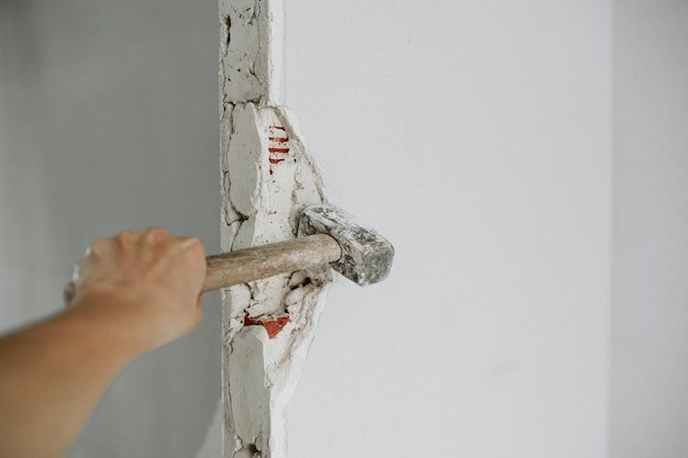 Unerkennbare Person hält einen Hammer, um eine Mauer auf der Baustelle zu zerstören