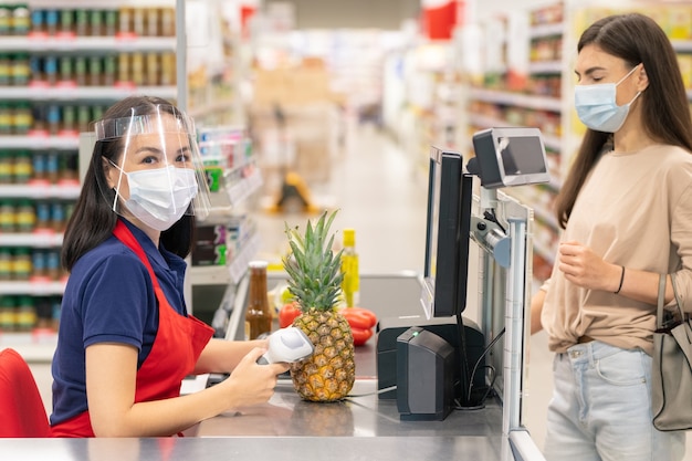 Unerkennbare Supermarktkassiererin, die den Computer verwendet, um nach dem Soßenpreis zu suchen, den ihr Kunde kaufen wird