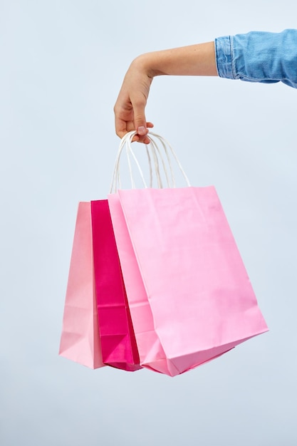 Unerkennbares Mädchen in lässigem Jeanskleid hält rosafarbene Einkaufstaschen in der Hand