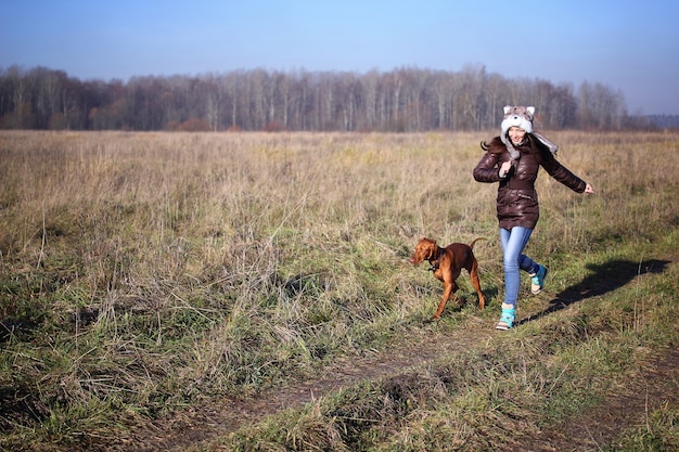 Ungarischer Vizsla-Hund und ein junges Mädchen in einem Hut, das auf dem Feld herumläuft