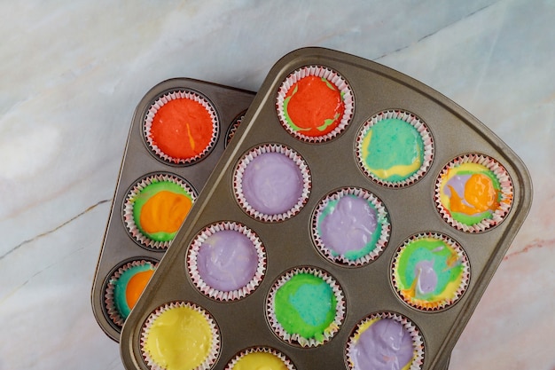 Ungebackene Regenbogen-Cupcakes auf zwei Backblechen. Ansicht von oben.