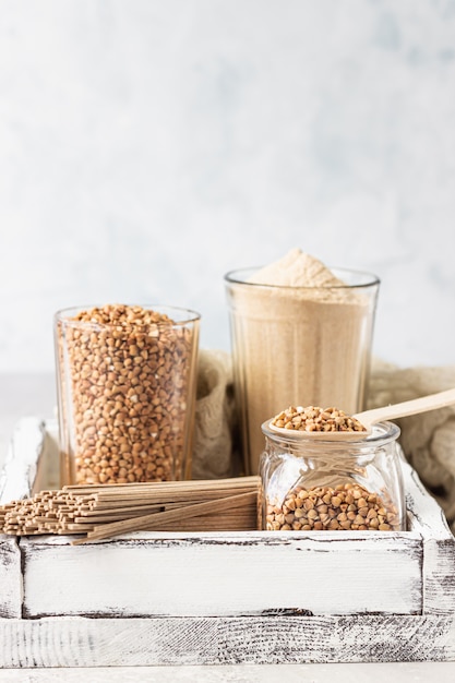 Ungekochte Bio-Buchweizenkörner, Buchweizenmehl und Buchweizen-Soba-Nudeln in einem Holztablett