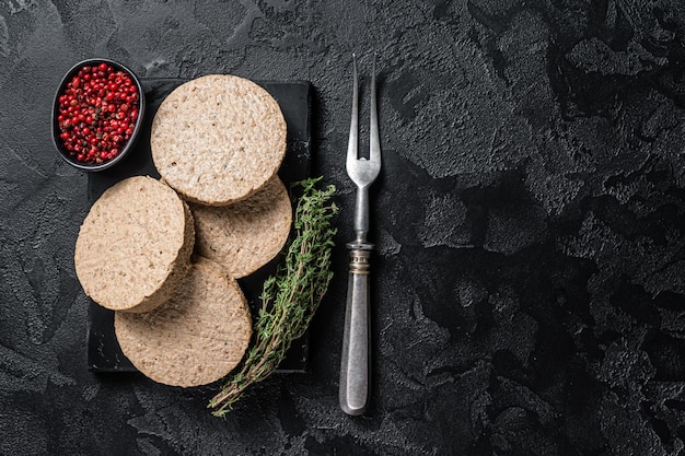 Ungekochte Burgerkoteletts aus pflanzlichem Fleisch, rohe vegane Patties. Schwarzer Hintergrund. Ansicht von oben. Platz kopieren.