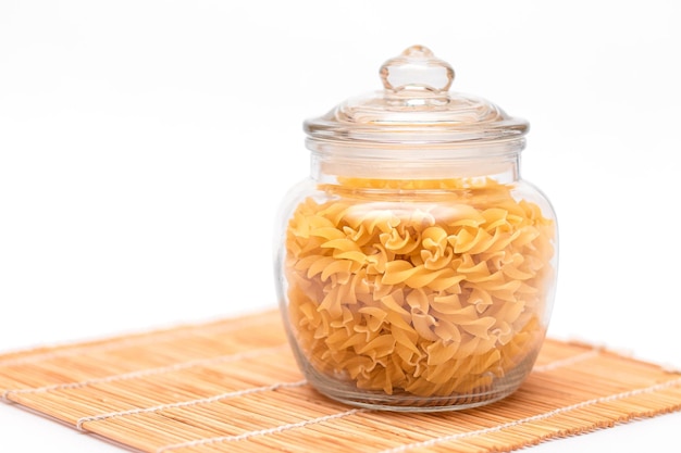 Ungekochte Fusilli-Nudeln im Glas auf weißem Hintergrund. Rohe und trockene Makkaroni. Ungesundes und fettes Essen. Italienische Kultur