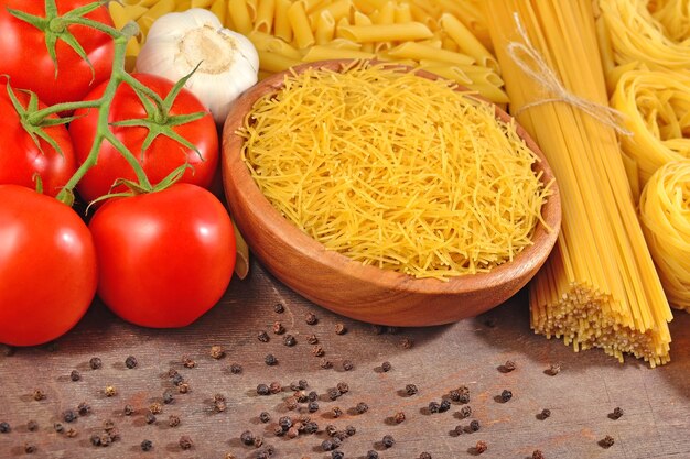 Ungekochte italienische Pasta, reife Tomatenzweige, Knoblauch und schwarzes P