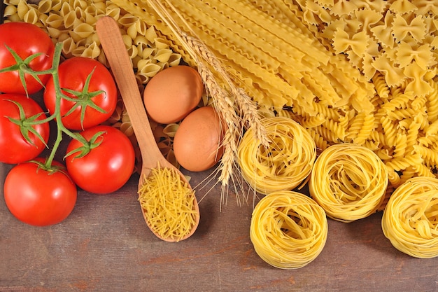 Ungekochte italienische Pasta, reife Tomatenzweige und Eier auf einem hölzernen Hintergrund