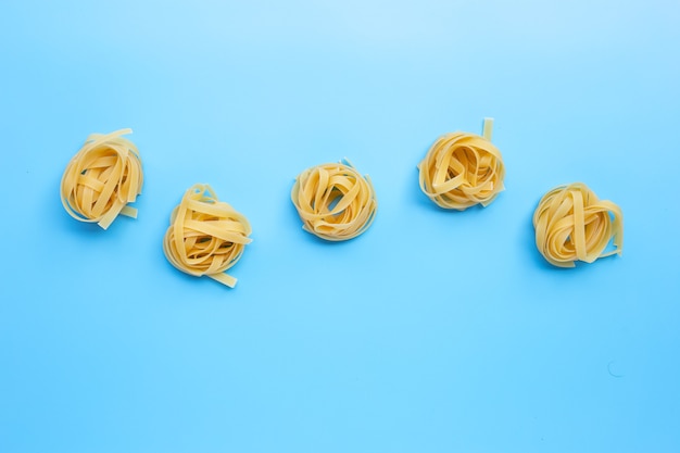 Ungekochte italienische Pasta Tagliatelle Nest auf blauer Oberfläche