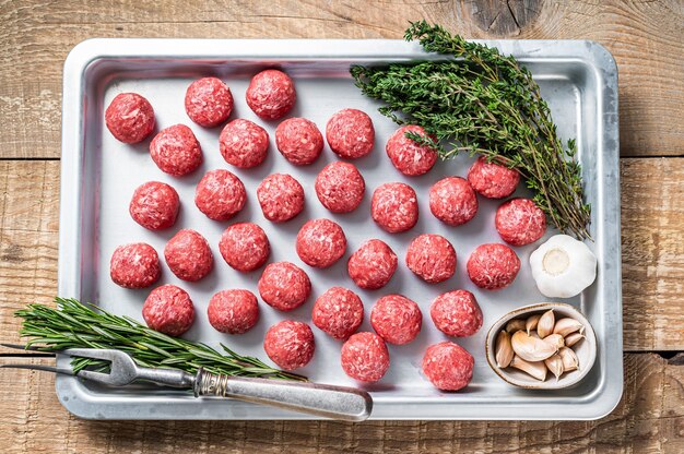 Ungekochte rohe rind- und schweinefleischbällchen mit thymian und rosmarin im küchentablett. holzhintergrund. draufsicht.