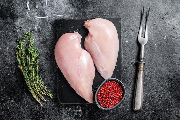 Ungekochtes Hähnchenbrustfilet, rohe Geflügelfleischsteaks. Schwarzer hölzerner Hintergrund. Ansicht von oben.