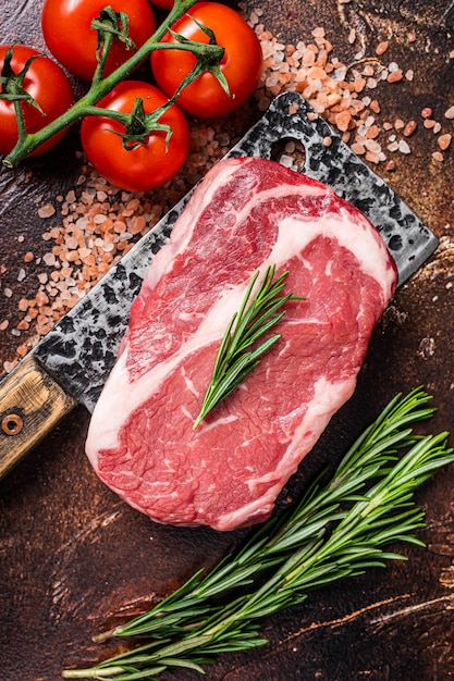 Ungekochtes rohes Rib-Eye-Steak Ribeye-Rindfleisch auf Metzgererbeil mit Kräutern Dunkler Hintergrund Ansicht von oben