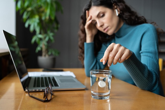 Ungesunde Frauen leiden unter Kopfschmerzen, Migräne im Büro, indem sie Aspirin-Schmerzmittel in Wasser auflösen