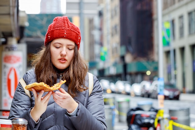 Ungesundes Essen und hübscher Mädchenjugendlicher des Straßenlebensmittels, mit nettem, mit Stück geschmackvoller Pizza