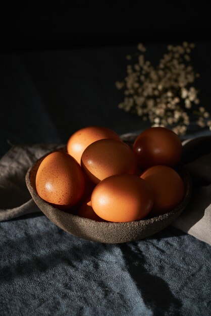 Ungewöhnliche Ostern auf dunklem Hintergrund. Schüssel mit braunen Eiern auf dunkelblauem Tisch, Blumen.