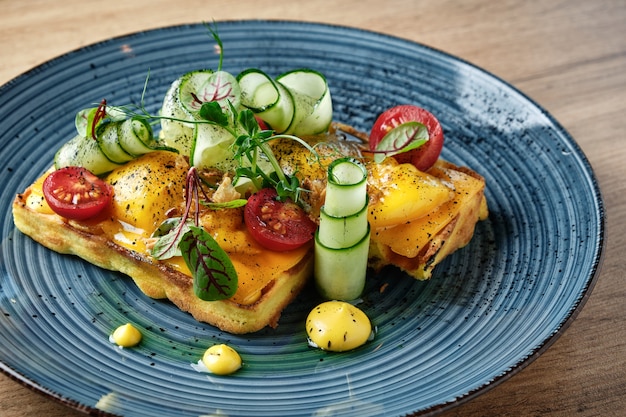 Ungewöhnliches Gericht ungesüßte Waffeln mit Kräuter-Tomaten-Gurke und Sauce auf einem schönen blauen Teller