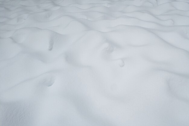Ungleichmäßiges weißes Schneeoberflächenmuster auf dem Boden mit Schneeverwehungen