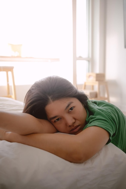 Unglückliche asiatische thailändische Frau, die sich auf einem weißen Husten-Sofa lehnt, während sie mit Traurigkeit mit dem Kopf auf dem Arm ruht
