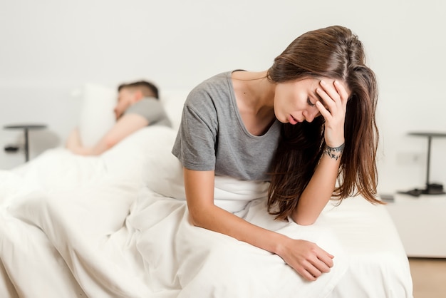 Unglückliche Frau im Bett mit einem schlafenden Mann. Konzept der Beziehung und der sexuellen Probleme