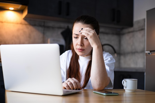 Foto unglückliche, gestresste geschäftsfrau, die schlechte nachrichten in der e-mail liest, frustrierte studentin, die an einem schwierigen online-projekt arbeitet, harte fernarbeit, arbeit im küchenbüro