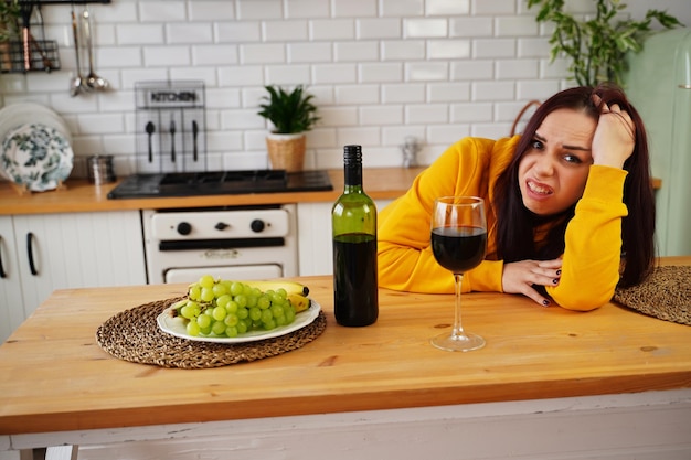Unglückliche junge Frau hat Kopfschmerzen von Rotwein Erwachsene Frau fühlt sich in der Küche schlecht von Alkohol