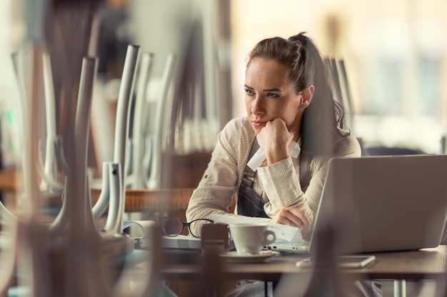 Unglückliche Kneipenbesitzerin sitzt über Computer und Kaffee und denkt darüber nach, was zu tun ist, da das Geschäft aufgrund einer Pandemie geschlossen bleiben muss