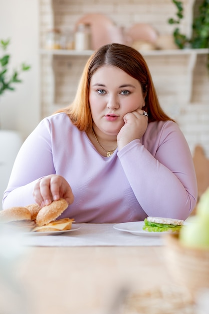 Unglückliche mollige Frau, die sich die Wange hält, während sie einen Hamburger nimmt