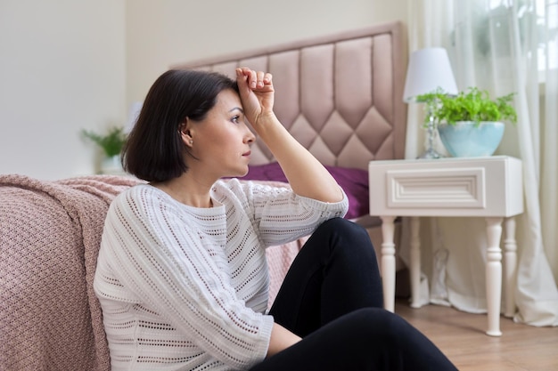 Unglückliche, müde, depressive, reife Frau, die zu Hause auf dem Boden sitzt