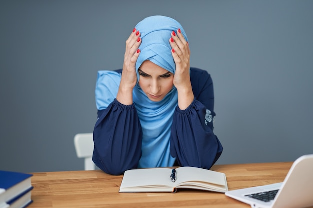 Unglückliche muslimische Studentin, die in der Bibliothek lernt