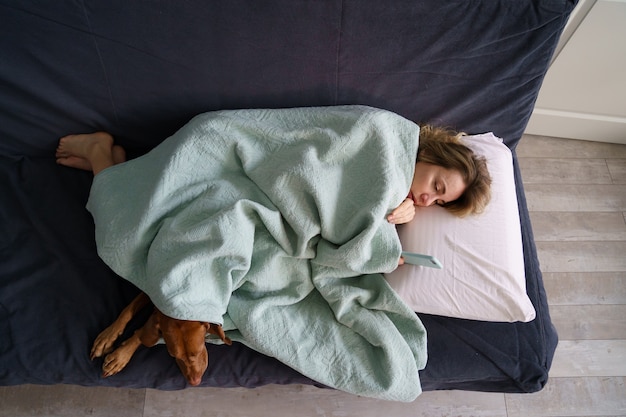 Unglückliche weinende Frau las Nachricht von Exfreund, der auf Sofa mit Decke bedeckt mit Hund liegt