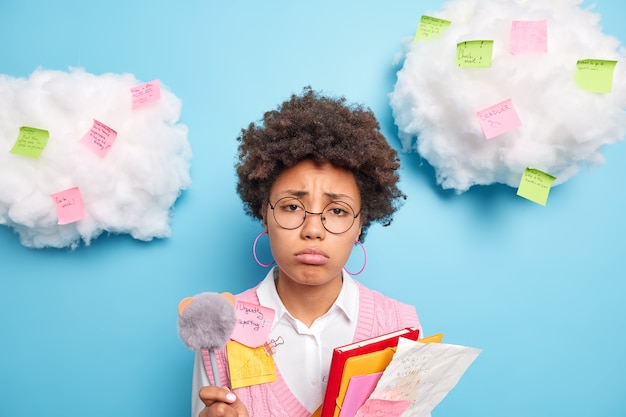 Unglücklicher unzufriedener schüler fühlt sich sehr müde von der prüfungsvorbereitung hält stift notizblock und papiere posiert gegen weiße wolken mit bunten haftnotizen, um daran zu erinnern, was zu tun ist