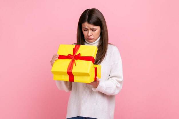 Unglückliches dunkelhaariges Mädchen, das nach innen schaut, verpacktes Geschenk, offenes Geschenk, das Enttäuschung ausdrückt