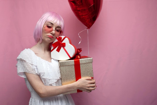 Unglückliches Mädchen mit rosa Haaren im Kleid hält Geschenke und Luftballons und ist traurige Frau ist allein