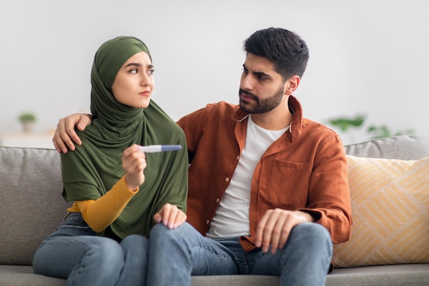Unglückliches Paar aus dem Nahen Osten mit negativem Schwangerschaftstest im Innenbereich